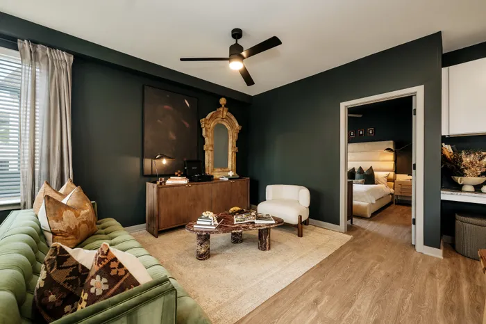 Chic and modern living room featuring a green velvet sofa, stylish decor, and natural light flowing through large windows, seamlessly connected to a cozy bedroom.