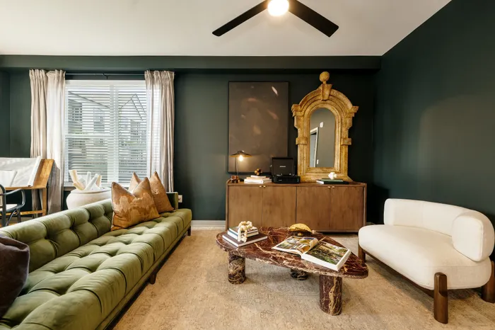 Elegant living room with a luxurious green velvet sofa, decorative pillows, and a modern marble coffee table, accented by a classic gold-framed mirror and warm wooden furniture.