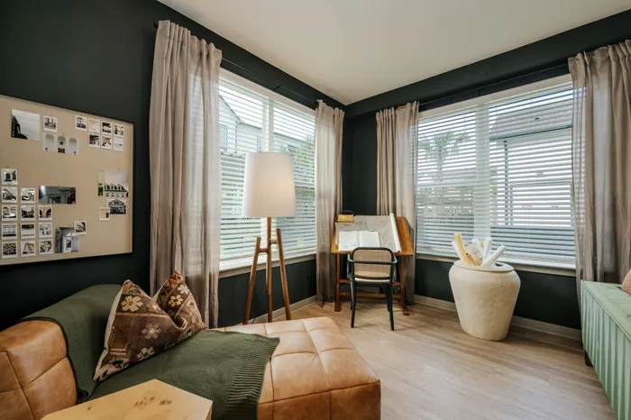 Cozy home office with large windows, elegant curtains, and stylish decor, featuring a leather chair, desk, and ambient lighting.