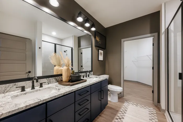 Modern and elegant bathroom with dark cabinetry, double sinks, and a spacious walk-in closet, exuding luxury and style.
