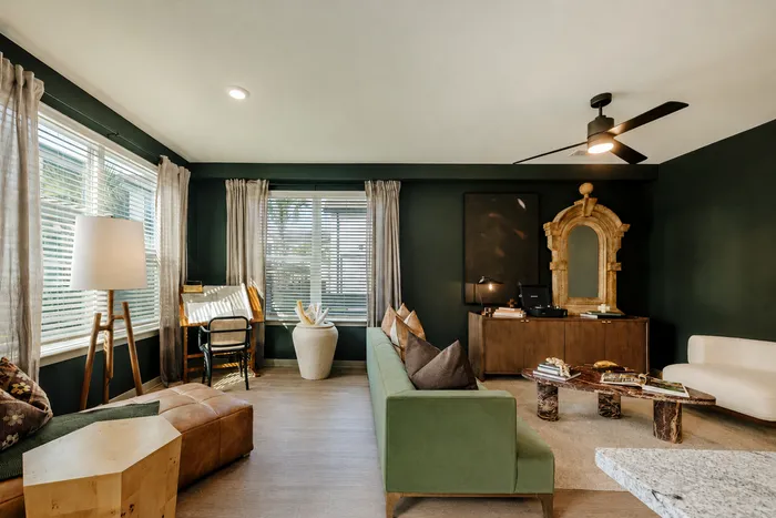 Elegant living room featuring dark green walls, trendy furniture, and natural light from large windows.