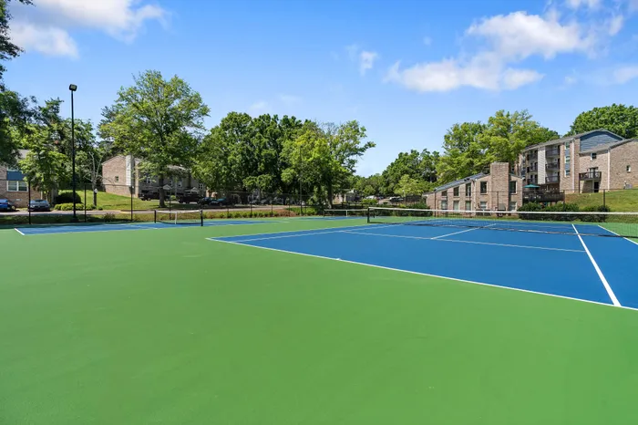 Vibrant tennis court surrounded by lush greenery and modern apartment buildings, offering a perfect blend of recreation and urban living.