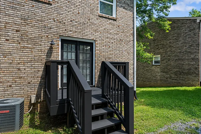 Charming brick exterior with elegant black stairs leading to a patio, surrounded by lush greenery.