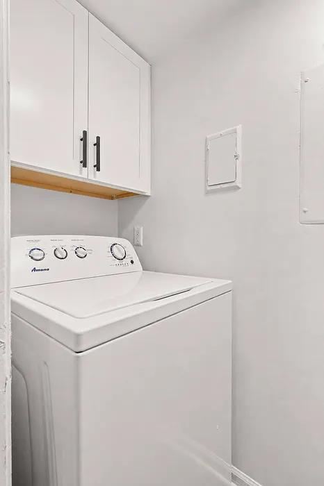 Chic apartment featuring a modern laundry area with a sleek washer and overhead storage cabinets.
