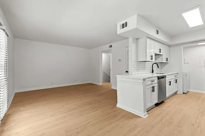 Bright and airy open-plan space featuring sleek hardwood floors and a modern kitchen with white cabinetry and stainless steel appliances.