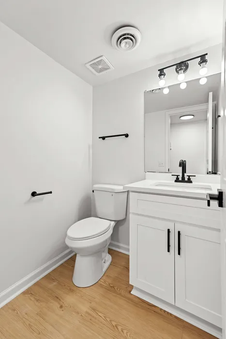 Modern bathroom featuring sleek white cabinetry, a pristine toilet, and elegant lighting with black fixtures, set against stylish wood flooring.
