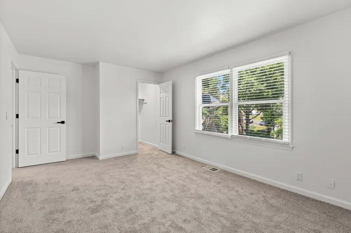 Bright, spacious bedroom with plush carpeting and large windows offering natural light and serene garden views.