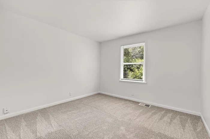 Bright and airy room with fresh carpeting and a large window overlooking lush greenery, perfect for relaxation.