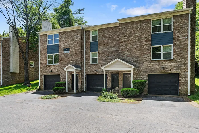 Charming multi-level townhouse with two entrances, lush greenery, and spacious driveways, showcasing classic brick architecture.