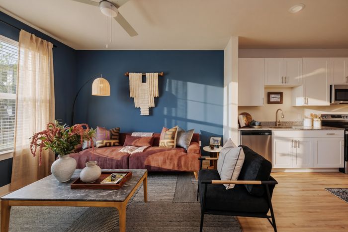 Chic apartment living room with plush sofa, elegant decor, and modern open-plan kitchen featuring white cabinetry and stylish appliances.