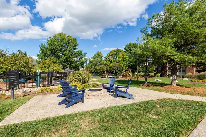 Charming outdoor seating area with blue Adirondack chairs around a fire pit, surrounded by lush greenery in a serene community setting.
