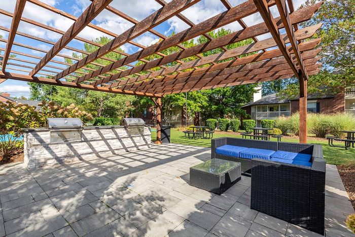 Charming outdoor patio with a wooden pergola, modern grills, and cozy seating area, perfect for entertaining and relaxation.