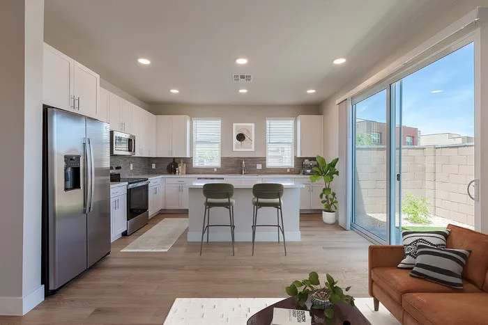 Bright and modern kitchen with sleek stainless steel appliances, elegant white cabinetry, and a spacious island perfect for casual dining, overlooking a cozy living area with natural light from sliding glass doors.