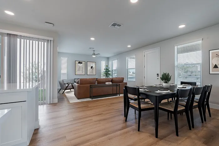 Modern open-plan living area with a stylish dark dining set, cozy leather couch, and bright natural light from large windows, perfect for entertaining.
