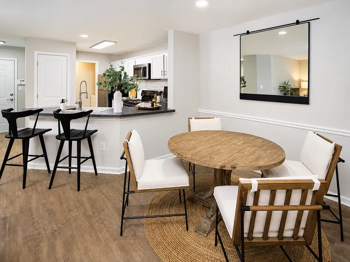 Modern apartment kitchen and dining area with sleek bar stools, a round wooden dining table, and contemporary decor for a stylish living experience.