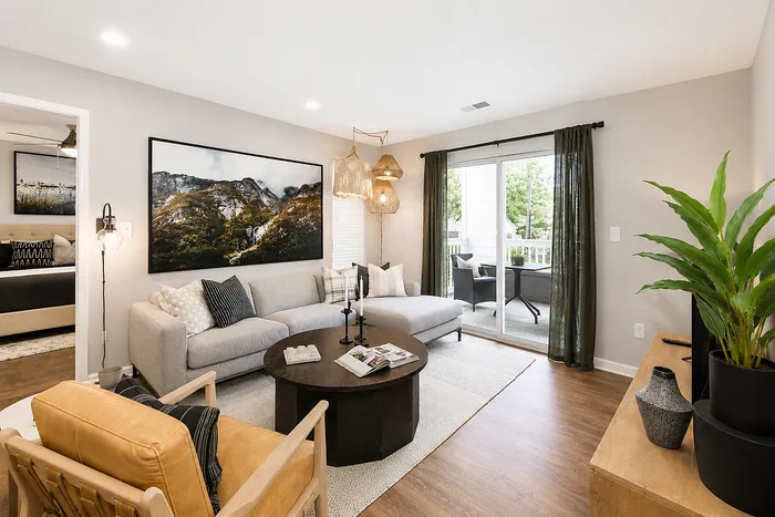 Elegant living room with a cozy sectional sofa, modern decor, and vibrant greenery opening to a serene balcony view.