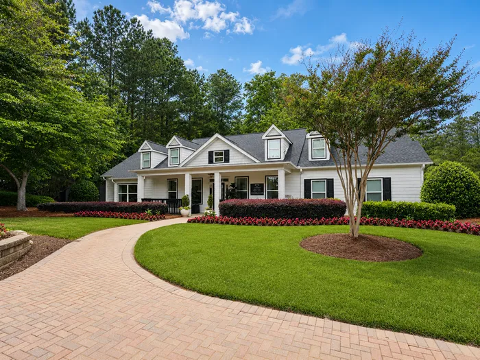 Charming single-story home with dormer windows, manicured landscaping, and a curved brick path leading to a welcoming front porch.
