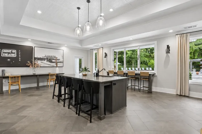 Spacious dining area featuring a sleek island with black stools, large windows allowing natural light, and modern decor with artistic wall accents.