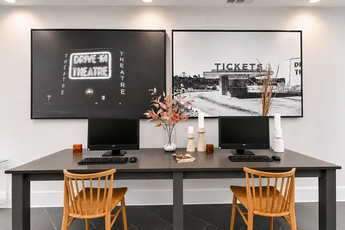 Chic and modern workspace featuring dual computer setup with stylish decor, framed vintage theater prints, and cozy wooden chairs.