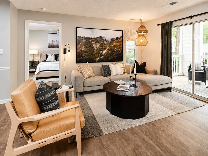 Inviting living room with elegant decor, plush sofa, cozy armchair, and large artwork; adjacent to a serene bedroom and balcony access.