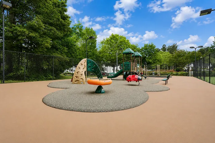 Vibrant playground with modern equipment, including slides and climbing structures, set in a lush, green park under a bright blue sky.