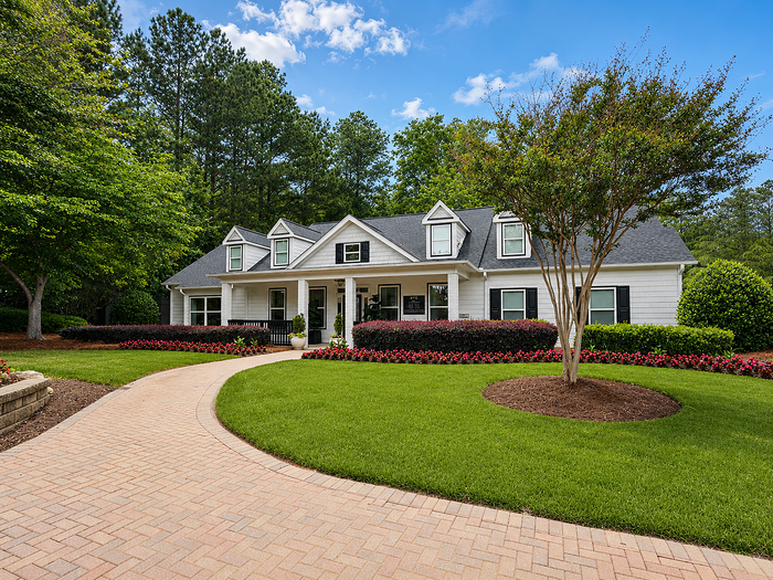 Charming suburban home with elegant white exterior, surrounded by lush greenery and vibrant flower beds, offering a peaceful and inviting atmosphere.