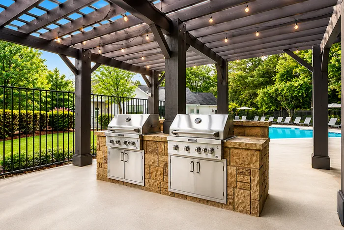 Luxurious outdoor kitchen featuring stainless steel grills under a stylish pergola, adjacent to a sparkling pool with sun loungers, surrounded by lush greenery.