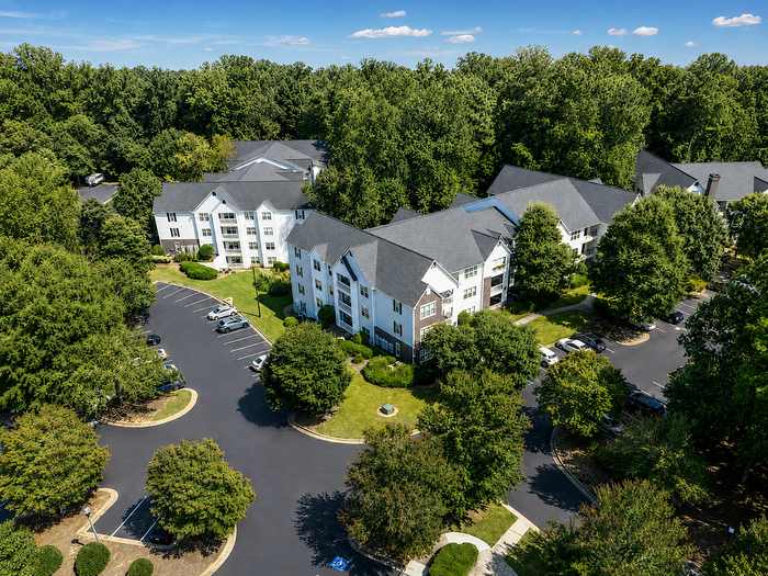 Aerial view of charming apartment complex nestled among lush greenery, offering serene living with ample parking and modern architecture.