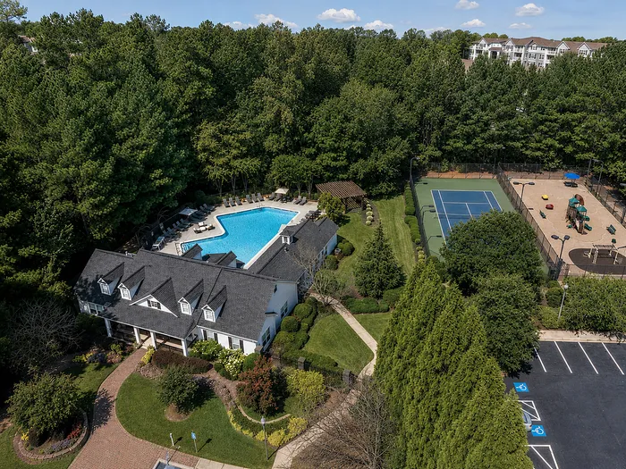 Charming aerial view of a community with a luxurious pool, tennis court, and playground, surrounded by lush greenery.