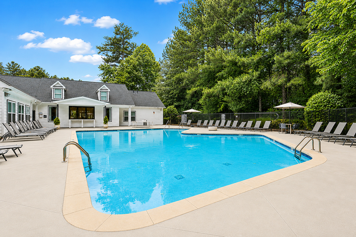 Inviting outdoor swimming pool with lounging area beside a charming clubhouse, surrounded by lush greenery.