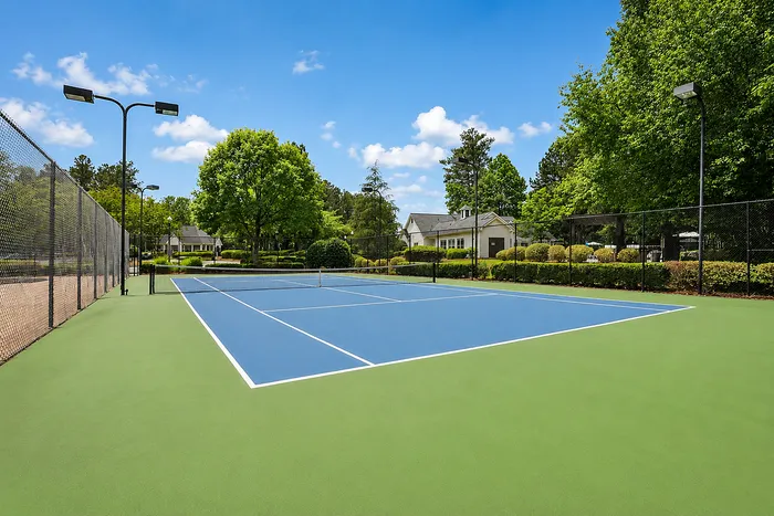 Beautiful outdoor tennis court surrounded by lush greenery and bright blue skies, perfect for recreation and relaxation.