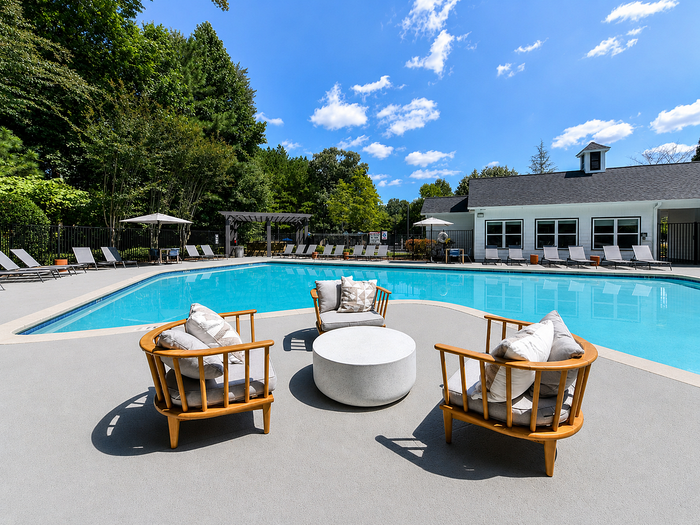 Luxurious poolside oasis featuring modern patio furniture, surrounded by lush greenery and a bright sky.