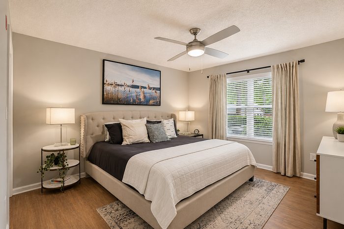 Chic and inviting bedroom with a plush bed, modern ceiling fan, elegant décor, and ample natural light streaming through large windows.