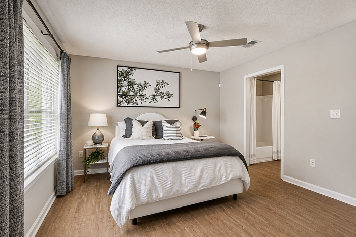 Chic bedroom with a plush bed, stylish decor, wooden floors, and abundant natural light streaming through large windows.