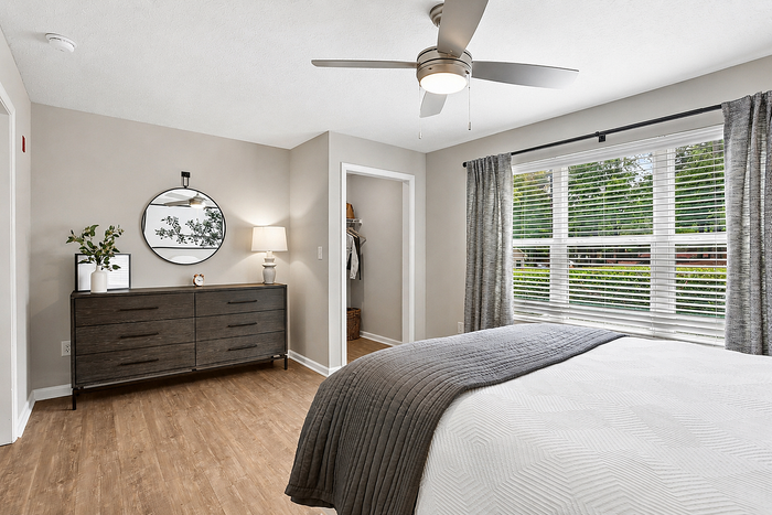 Bright and airy bedroom with modern decor, featuring a chic dresser, large window with lush greenery views, and elegant ceiling fan.
