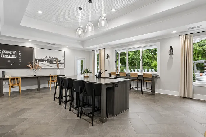 Elegant communal living space with modern island seating, sleek pendant lighting, and large windows offering scenic greenery views.