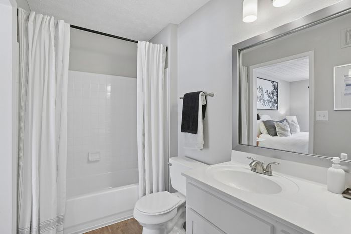 Bright modern bathroom with elegant fixtures, pristine white tiles, and a sleek vanity mirror reflecting a cozy bedroom.