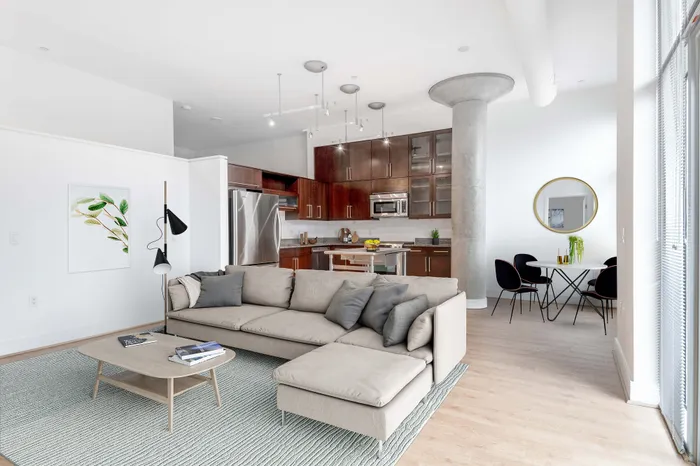 Modern apartment interior showcasing a sleek open-concept living area with a comfortable beige sectional sofa, stylish wooden flooring, and a contemporary kitchen with stainless steel appliances and rich wooden cabinetry.