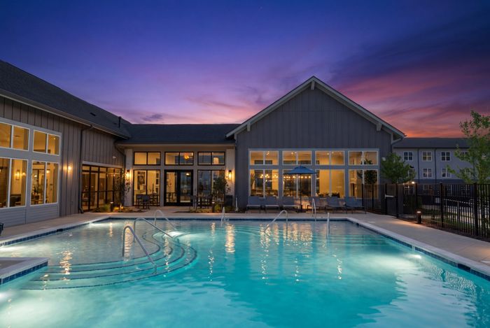 Luxurious resort-style swimming pool and clubhouse at sunset with illuminated water and outdoor lounge seating.