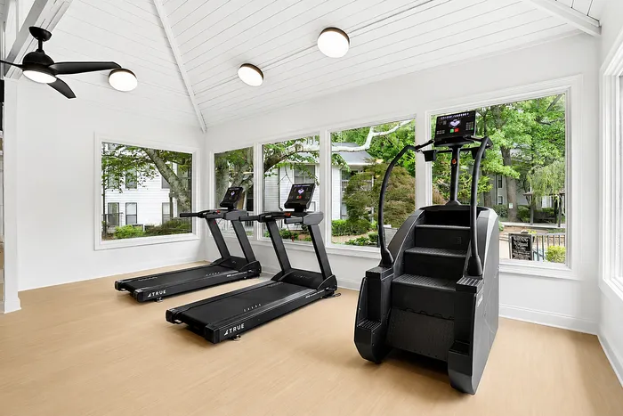 Bright, modern fitness room with floor-to-ceiling windows, two treadmills, and a stair-stepper, offering a refreshing workout experience.