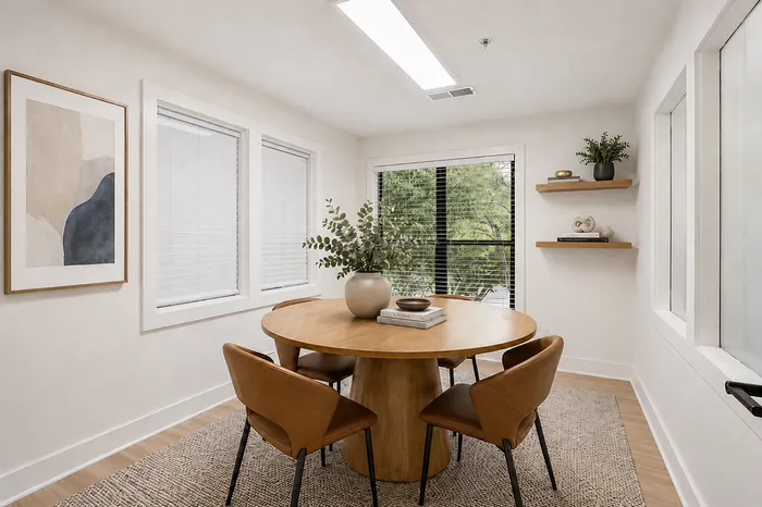 Bright dining area with a round wooden table, cozy leather chairs, modern decor, and natural light from large windows.