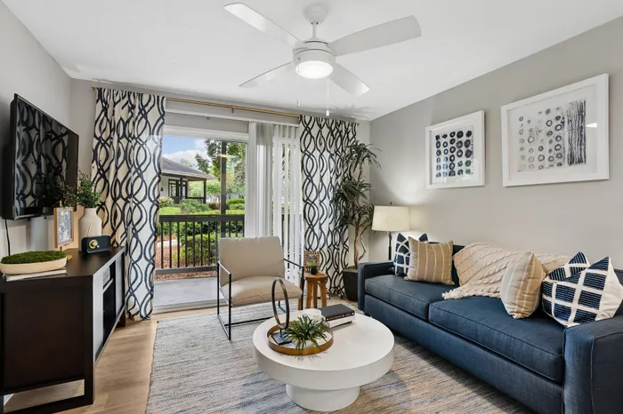 Elegant living room with a chic navy sofa, stylish decor, and a bright view of lush greenery through large sliding doors.