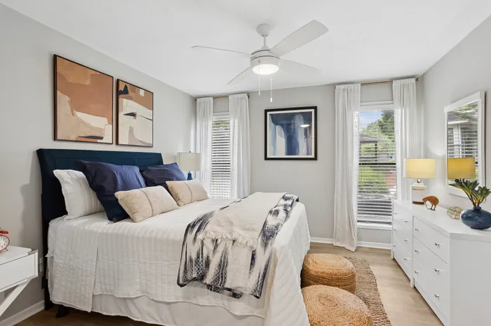 Elegant bedroom featuring modern decor, a cozy bed with plush pillows, and natural light streaming through wide windows accented by sheer curtains.