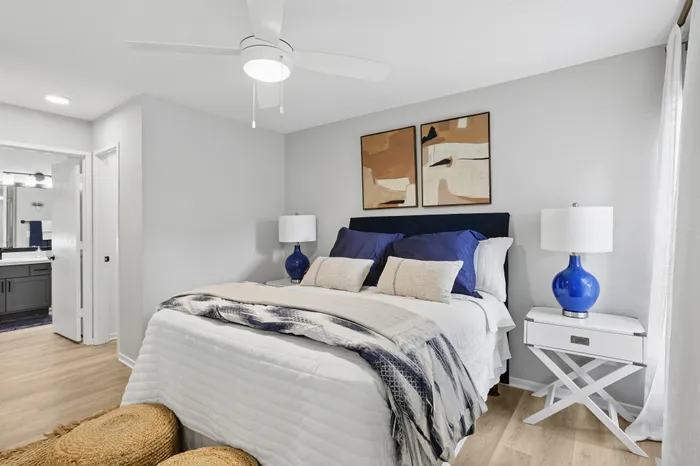 Elegant bedroom with modern design, featuring cozy blue and white accents, stylish artwork, and a bright ambiance.