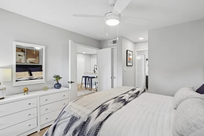 Bright and modern bedroom with stylish decor, ceiling fan, and comfortable bedding, providing a serene space with seamless access to a chic dining area.