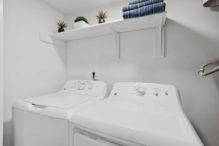 Modern laundry room featuring a pristine white washer and dryer set, complemented by elegant shelves with decorative plants and neatly stacked towels.