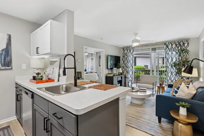 Modern apartment interior showcasing an open kitchen with sleek cabinetry, vibrant living area with stylish decor, and large windows letting in natural light.