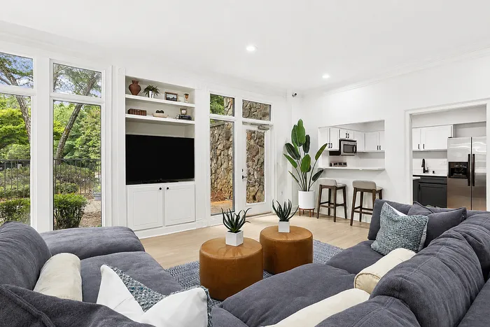 Bright and inviting living area with modern decor, featuring large windows, a built-in entertainment center, and an open kitchen with sleek appliances.