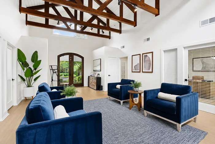 Elegantly designed living room featuring bold blue armchairs, natural wood flooring, and modern decor under stunning exposed wooden beams.