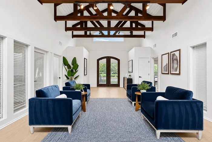 Bright, spacious living room featuring elegant exposed wooden beams, plush navy blue sofas, and a lush green view through large glass doors.